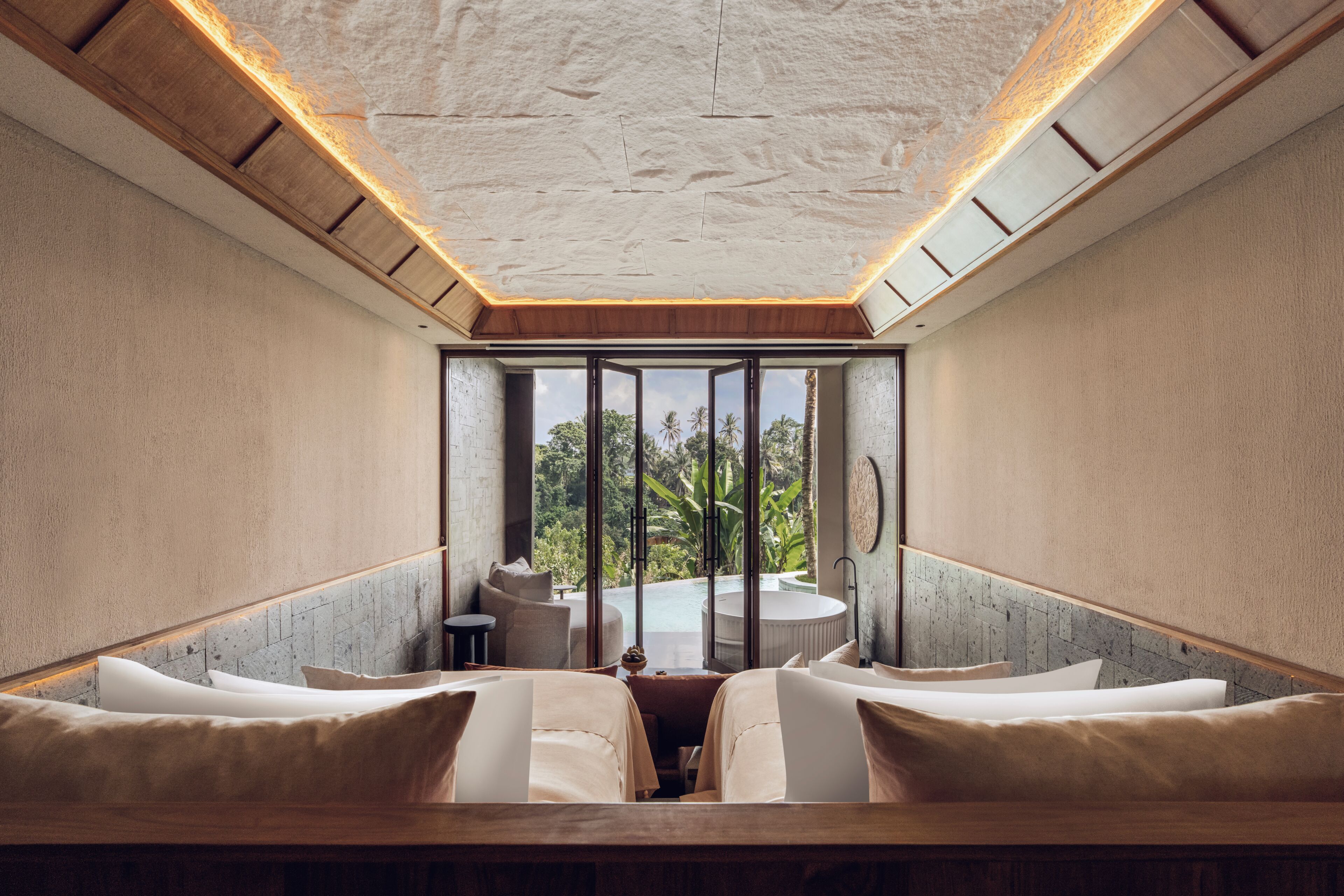 A room with a large window, a wooden ceiling, and a seating area with white cushions.