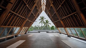 Amplia habitación con techo alto, estructura de celosía de madera y ventanas grandes que dan a vistas de palmeras.