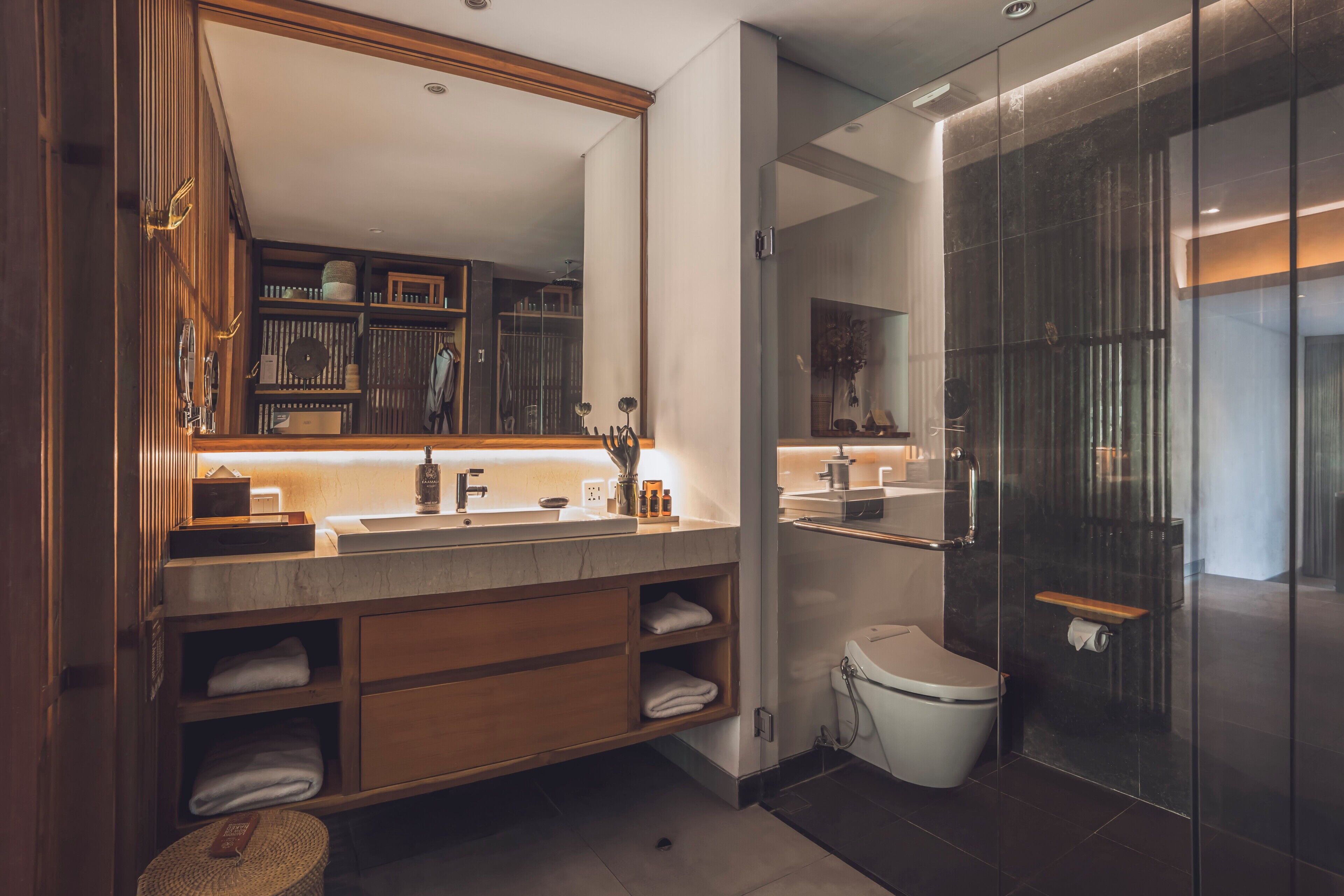A modern bathroom with a wooden vanity, a large mirror, a glass shower enclosure, and a toilet.