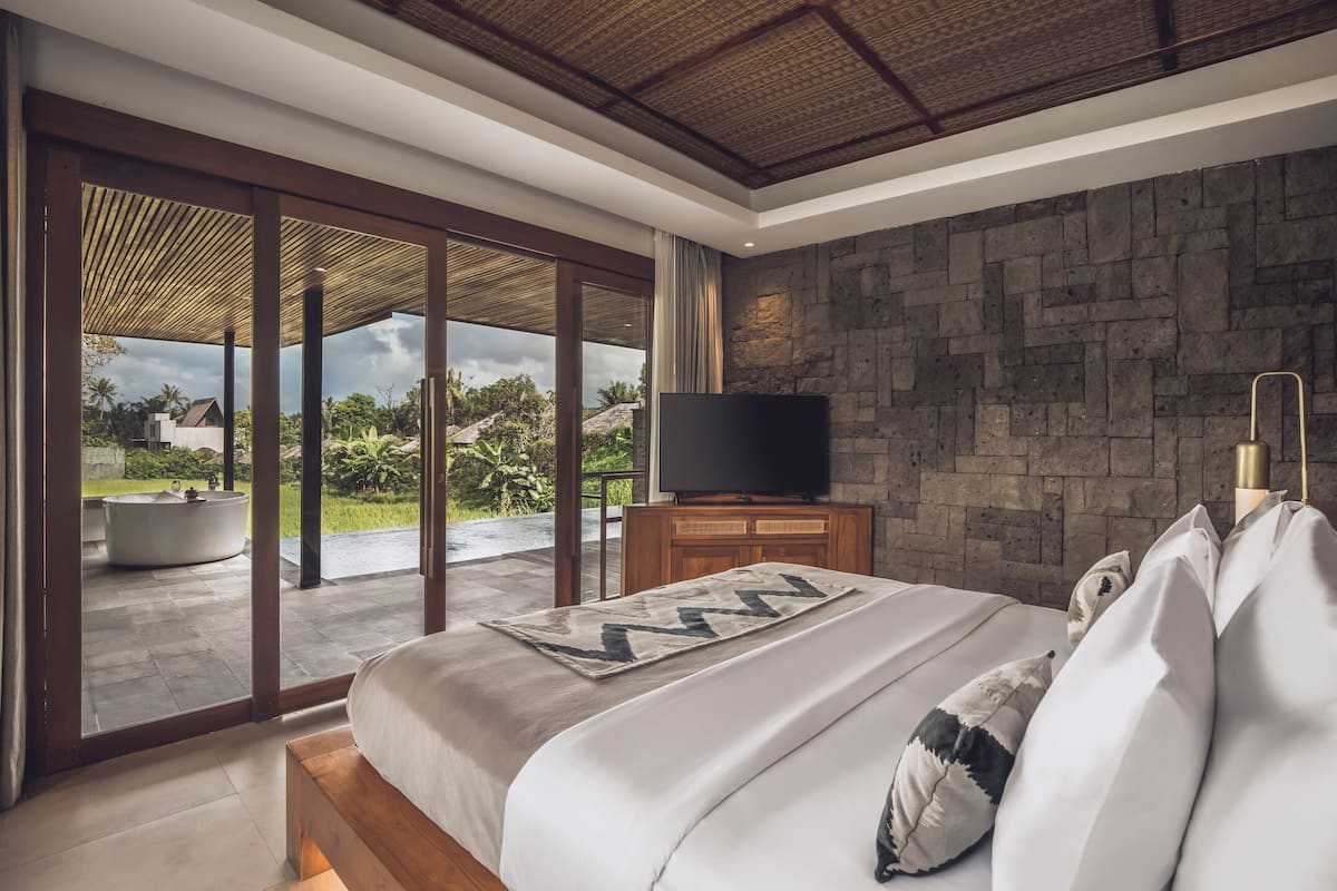 A modern bedroom with a large bed, a TV, and a stone wall.