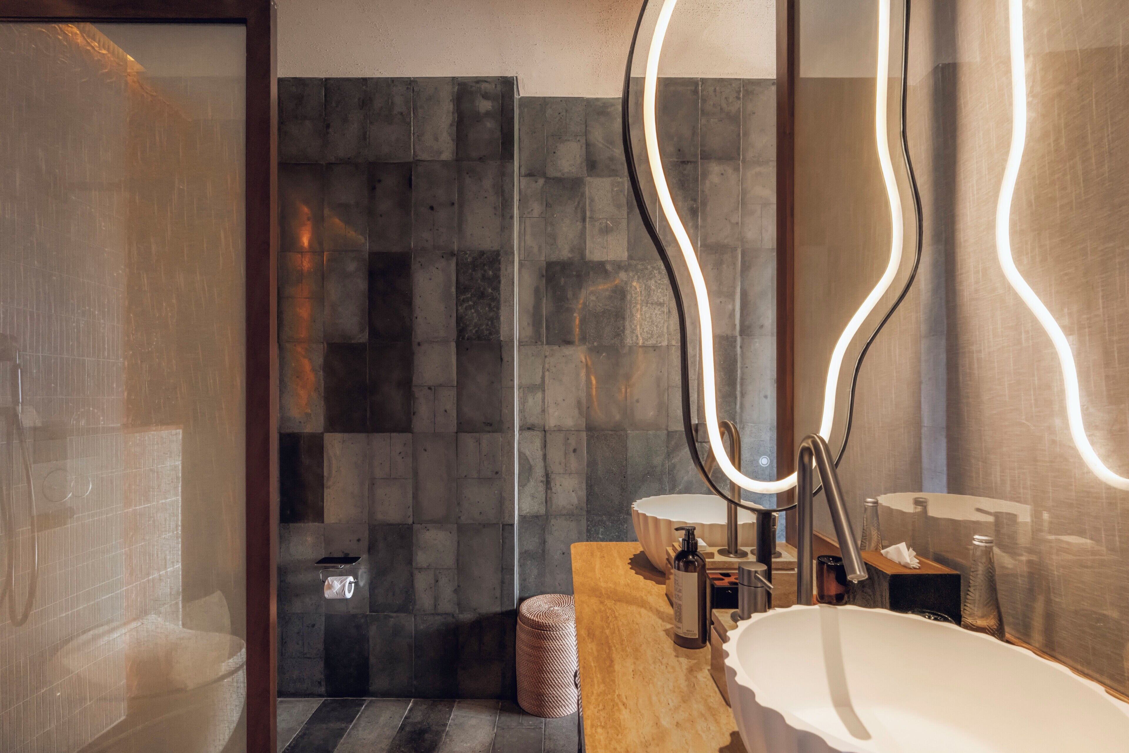 A modern bathroom with a freestanding bathtub, a large mirror with integrated lighting, and a shower area with a textured wall.