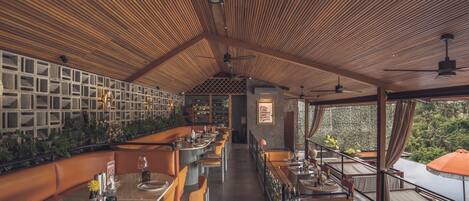 Un restaurante con techo alto, vigas de madera y una barra larga con sillas anaranjadas.