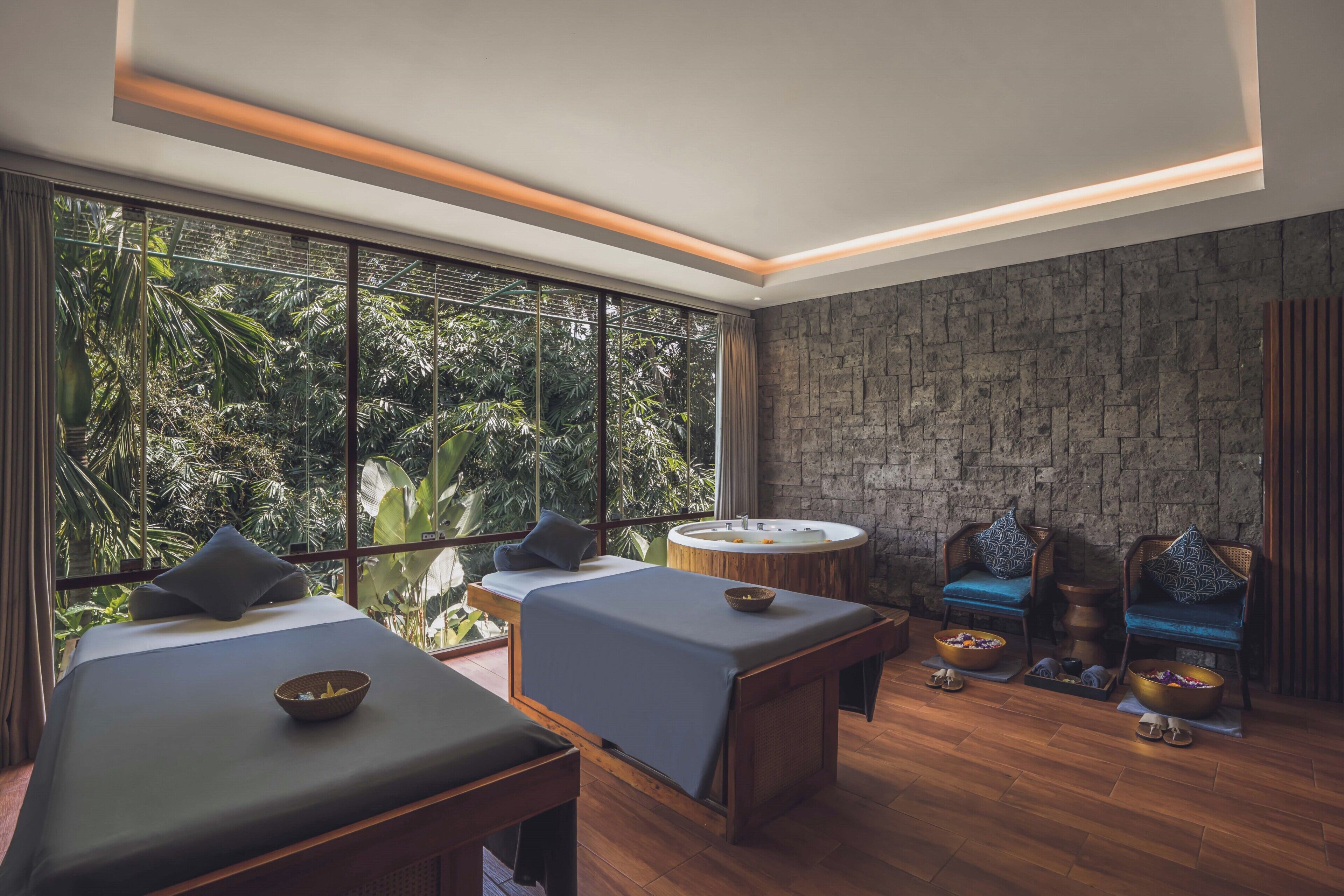 Une salle de spa équipée de deux tables de massage, d’un jacuzzi rond et d’un mur en pierre.