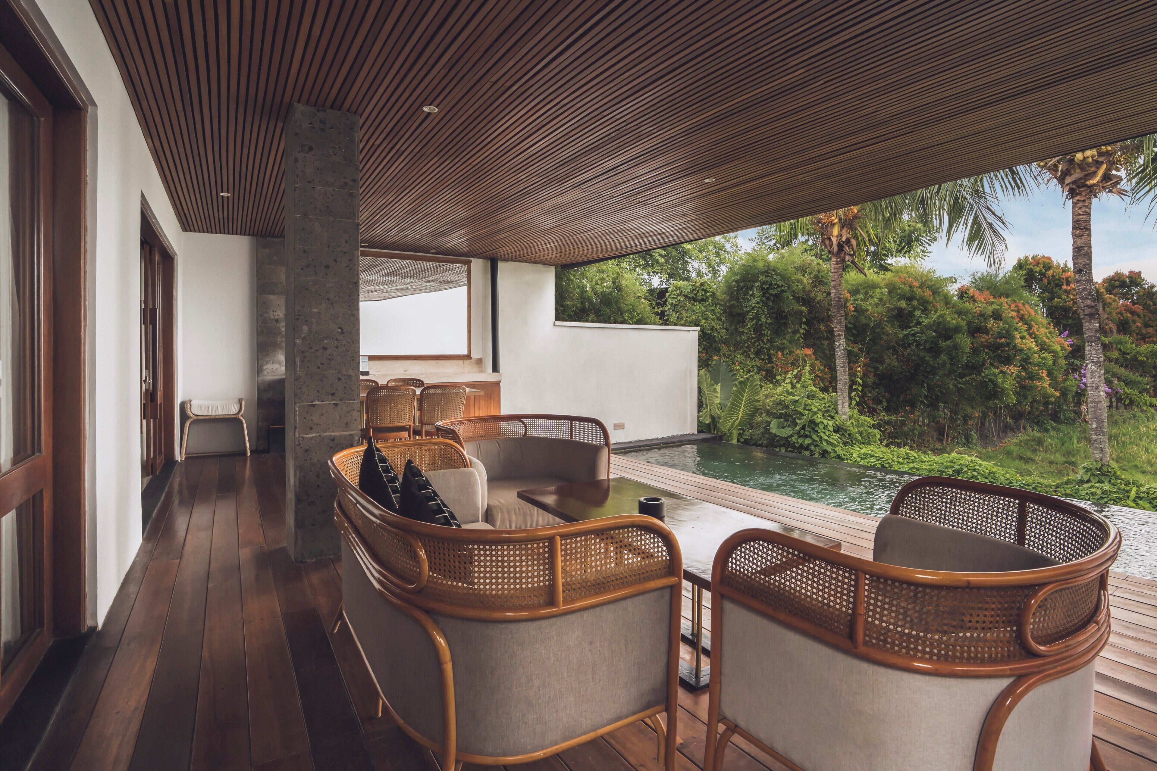 A wooden deck with wicker furniture overlooking a pool and lush greenery.