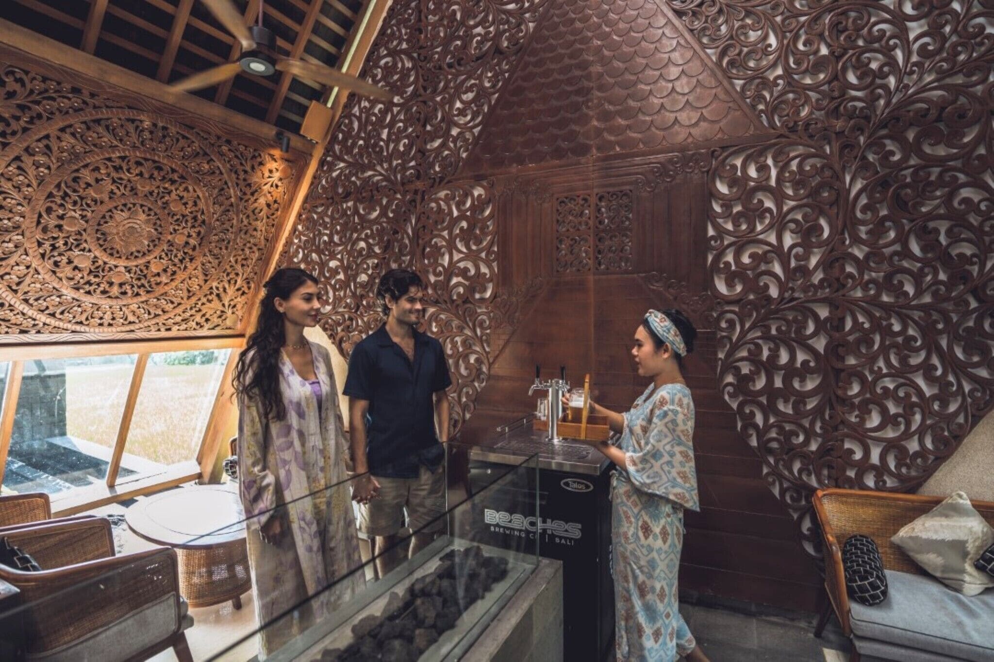 An interior with ornate wooden carvings, a glass display case, and a seating area with wicker furniture.