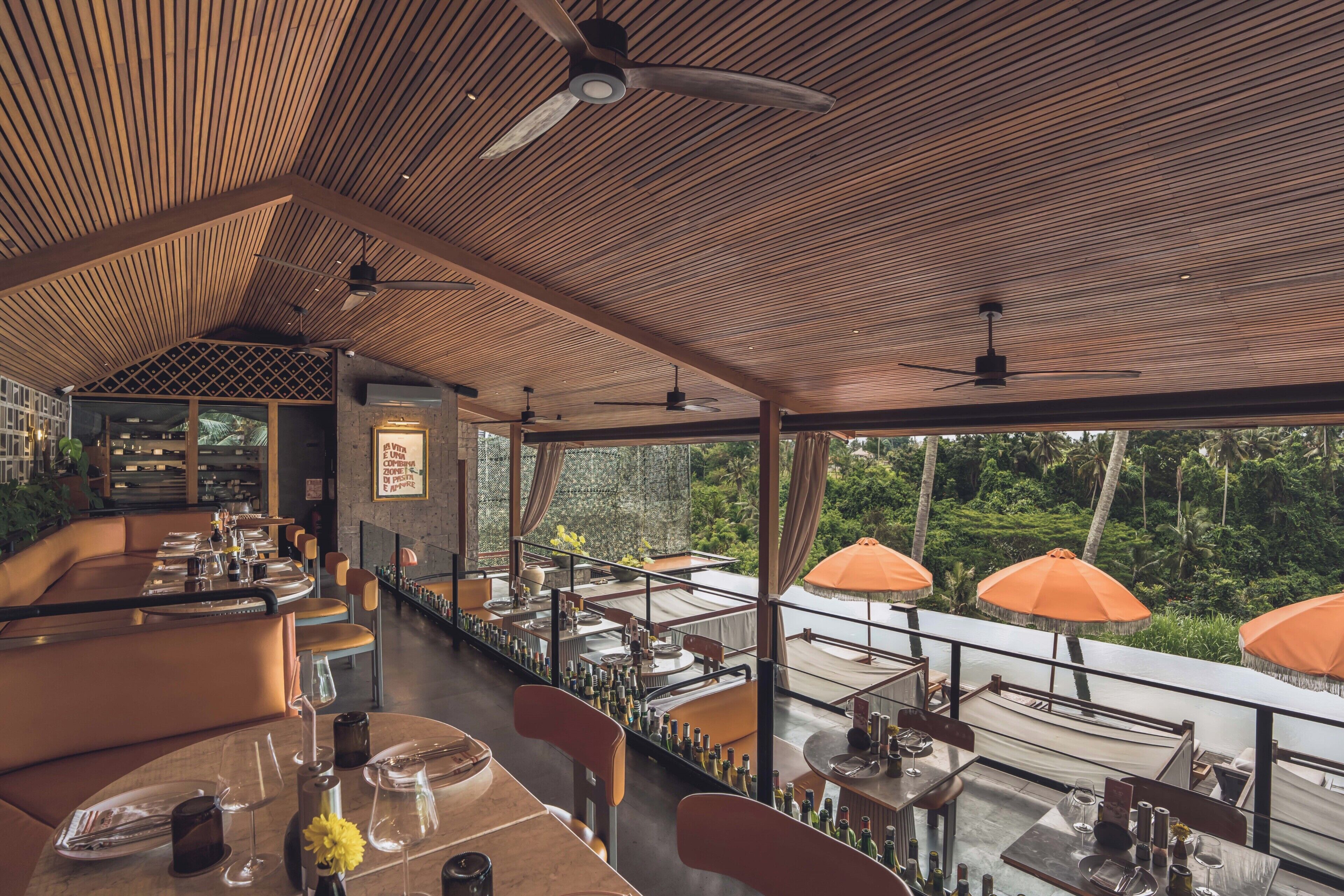 Un restaurante con techo de madera, mesas con sillas y sombrillas exteriores.