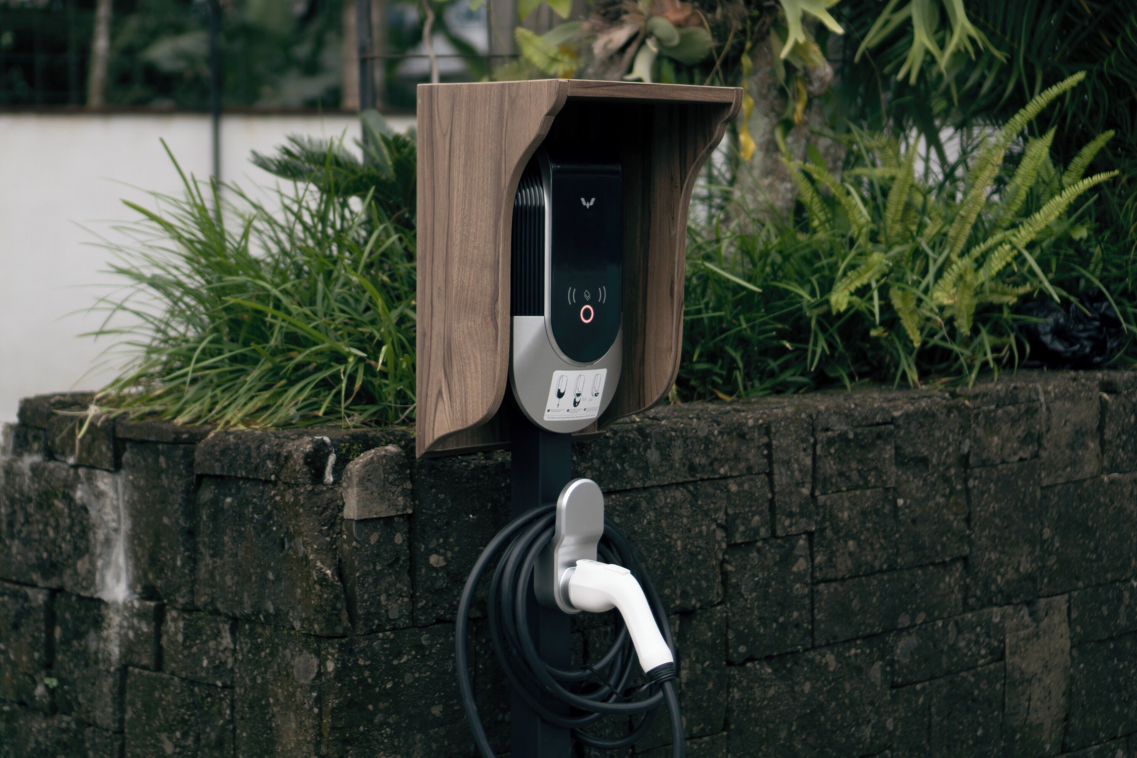 An electric vehicle charging station with a wooden housing, a digital display, and a cable connected to a wall-mounted charging point.