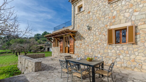 Un edificio de piedra con balcón, asientos al aire libre y vistas del paisaje circundante.