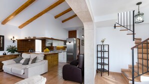 Un amplio salón con sofá, una silla, una cocina con electrodomésticos modernos y una escalera con un farol.
