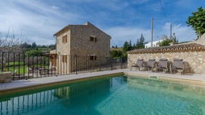Un edificio de piedra con piscina, mobiliario exterior y un patio vallado.