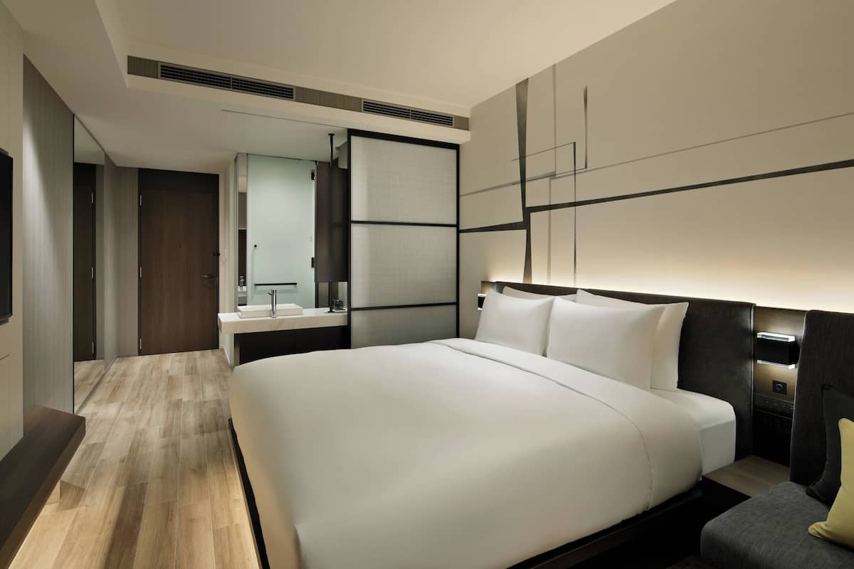 Een moderne hotelkamer met een groot bed, nachtkastje, spiegel en een ingebouwde televisie.