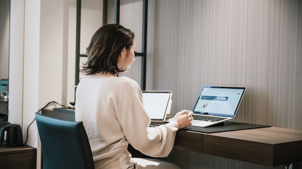 A person working at a desk with two laptops, a coffee maker, and a modern office chair.