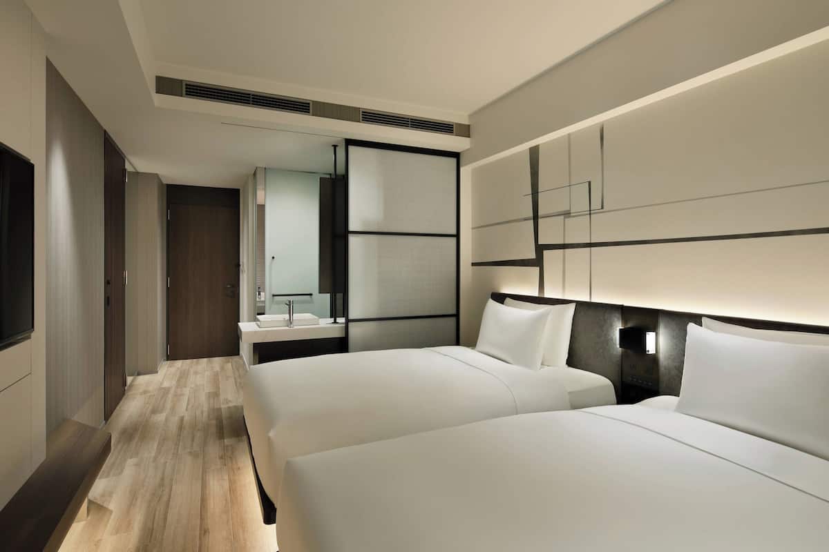 Een moderne hotelkamer met twee bedden, een grote spiegel, een nachtkastje en een ingebouwde kachel.