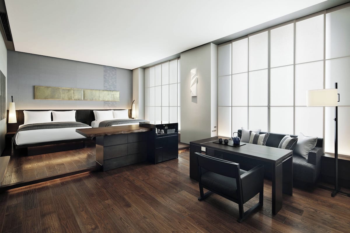 Een moderne hotelkamer met een bed, een bureau, een bank en een groot raam.