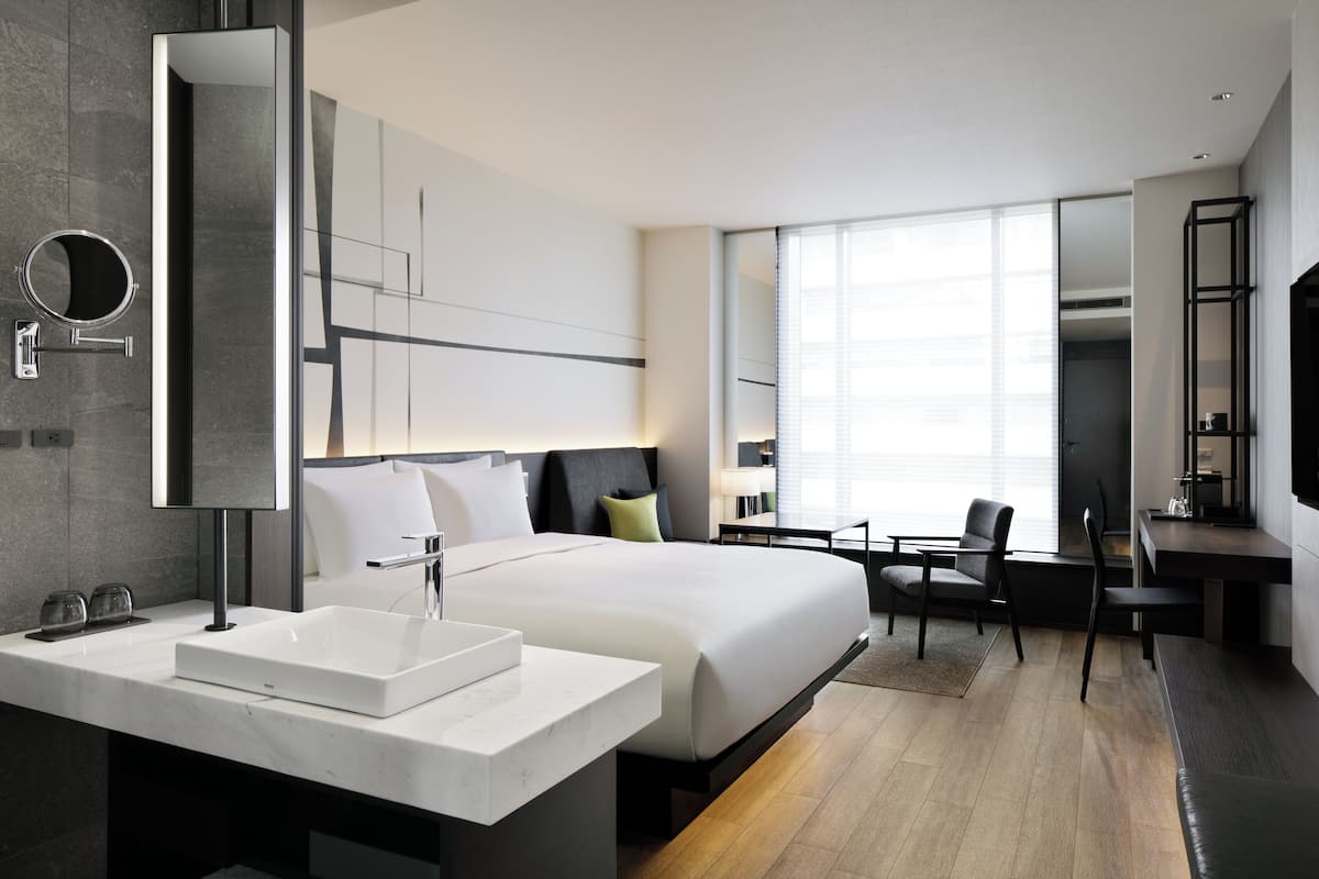 Een moderne hotelkamer met een groot bed, een badkamer met een witte wastafel en een bureau met een stoel.