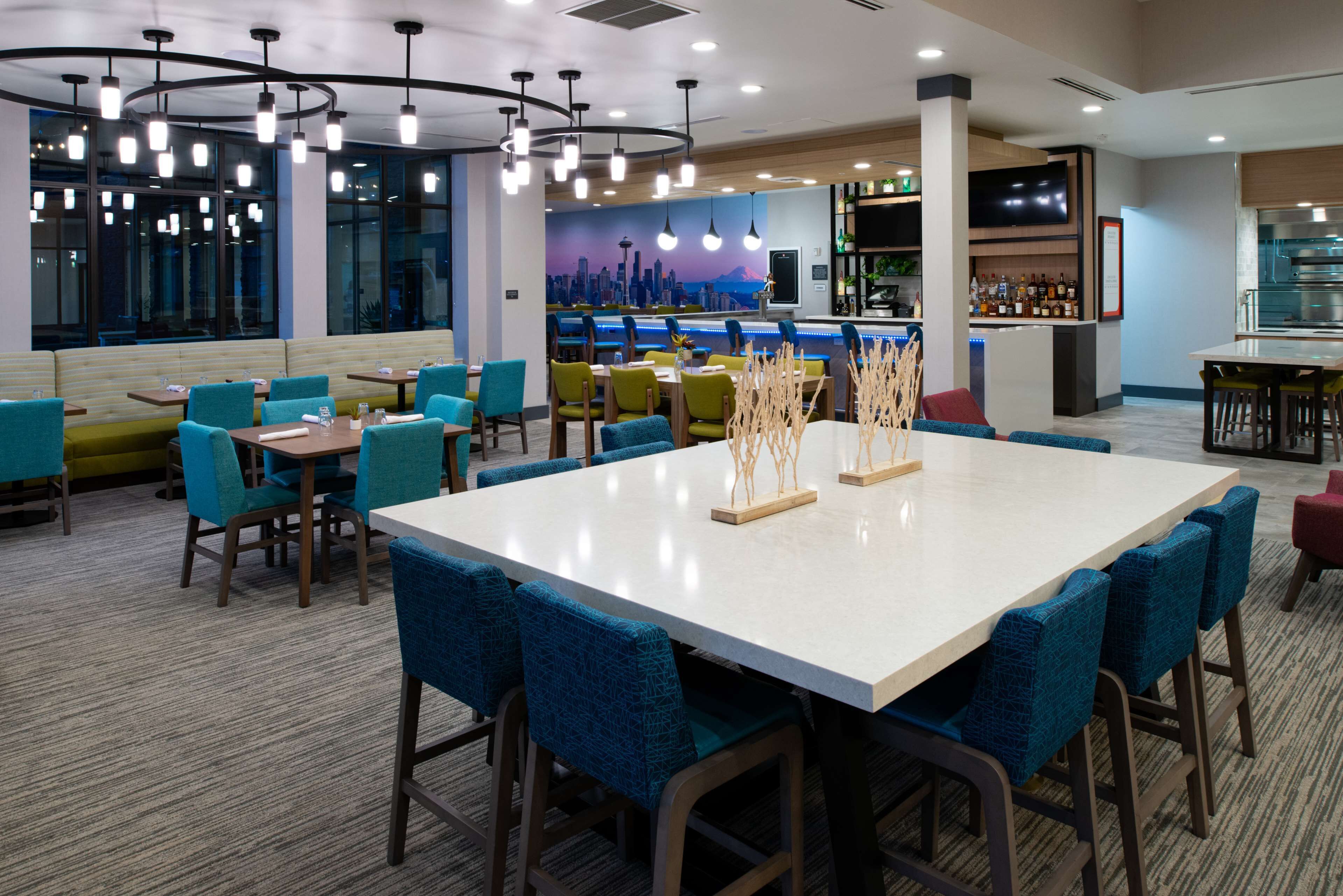 A modern restaurant with a large white table, blue upholstered chairs, and a cityscape mural on the wall.