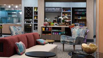 A modern lounge area with seating, a coffee shop in the background, and a kitchen area.