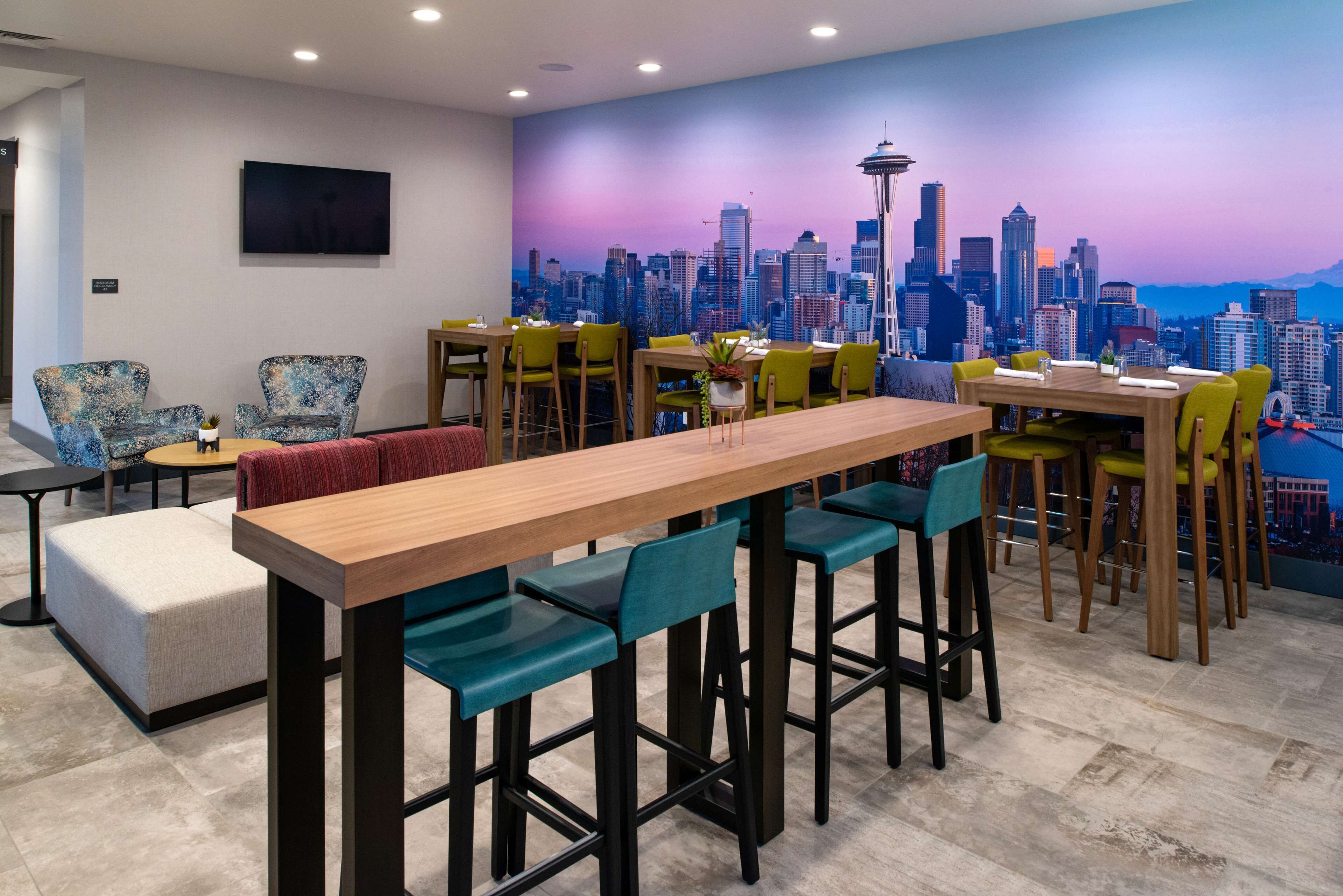 Un comedor moderno con un mural de la ciudad, una mesa de madera larga y sillas coloridas.