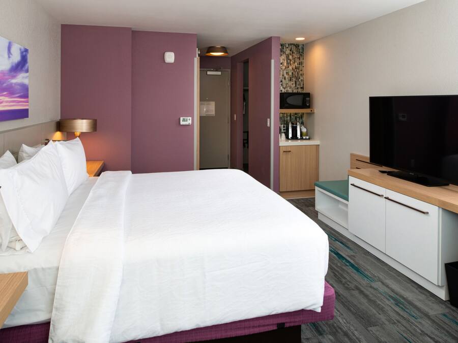 A hotel room with a large bed, a television, a desk, and a kitchenette area.