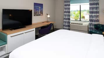 Une chambre d’hôtel avec un lit, un bureau avec une télévision, une chaise et une fenêtre avec des rideaux.