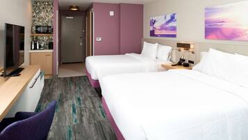 A hotel room with two beds, a desk with a computer, a microwave, and a small kitchenette.