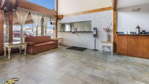 A hotel lobby with a sofa, a small table, a mirror, and a wooden counter. - Rodeway INN Rockford (Rockford)