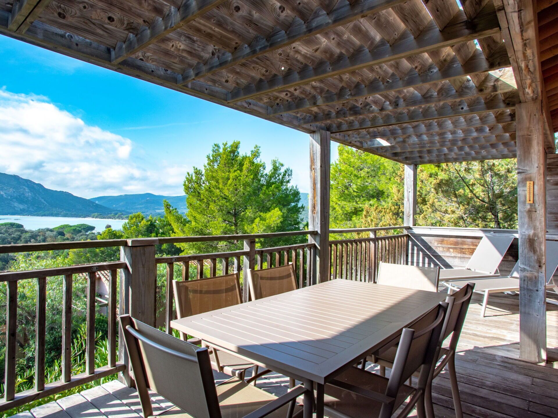 Une terrasse en bois avec une table et des chaises, d’où l’on a vue sur un lac et des montagnes.