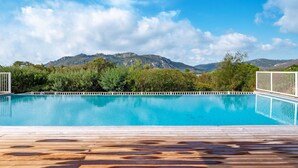 A swimming pool with a wooden deck in the foreground and a mountainous landscape in the background. - Lovely apartment in villa for 6 people with WIFI, A/C, pool, TV and terrace (Porto-vecchio)