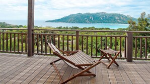 A wooden deck with two wooden lounge chairs facing a scenic view of a coastal landscape with mountains and the sea. - Lovely apartment in villa for 6 people with WIFI, A/C, pool, TV and terrace (Porto-vecchio)