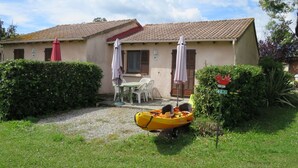 Edifici de dues plantes amb teulada de rajola, un petit pati amb taula i cadires, i un kayak groc al primer pla.
