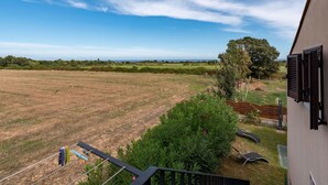 Une vue depuis un balcon donnant sur un champ verdoyant, avec un arbre et un bâtiment aux volets fermés.