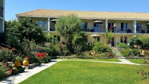 A two-story building with a tiled roof, a central garden with a lawn and various plants, and a staircase leading to the upper floor. - Cosy apartment for 2 guests with pool, A/C, WIFI and terrace (Calvi)