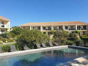 Um hotel com piscina, rodeado por vegetação e um céu azul límpido.