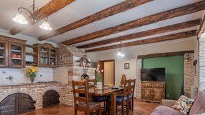 Ein rustikales Interieur mit freiliegenden Holzbalken, einem Steinofen, einer Essecke mit Holzsesseln und einem Fernseher in einem grün gestrichenen Raum.