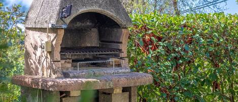 Un forno esterno in pietra con canna fumaria, immerso nel verde.