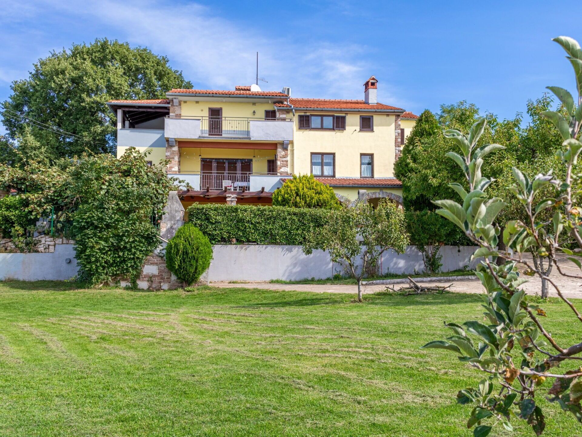 A two-story house with a balcony, surrounded by a well-maintained lawn and greenery.