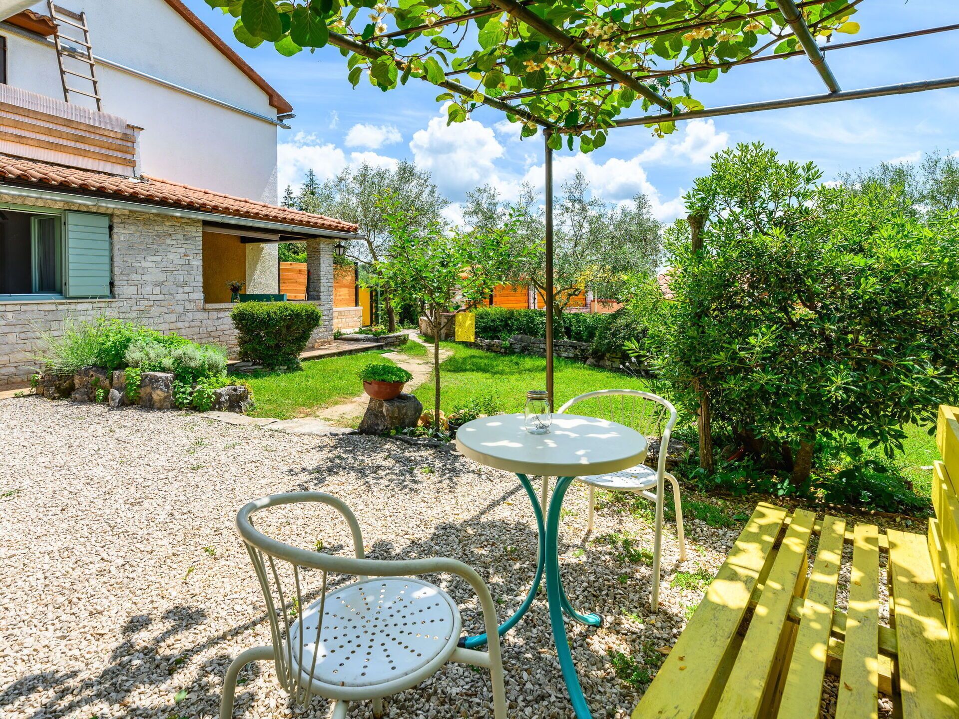 Une terrasse avec une table et des chaises, un banc en bois et un chemin de pierres menant à une maison.
