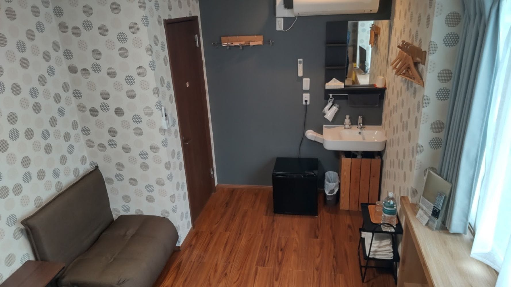 A compact living space with a sofa, a small black cabinet, a wooden bench, a sink, and a mirror.