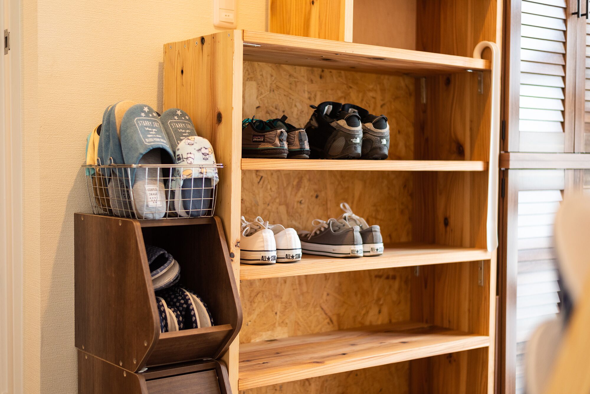 A wooden shoe rack with multiple shelves holding various pairs of shoes and a wire basket with folded clothes.