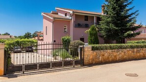 A pink two-story building with a tiled roof, a stone wall, and a metal gate. - Cosy apartment for 3 guests with pool, A/C, WIFI, TV and terrace (Porec)