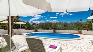 A swimming pool with a stone-tiled deck, surrounded by white lounge chairs and umbrellas. - Cosy apartment for 3 guests with pool, A/C, WIFI, TV and terrace (Porec)