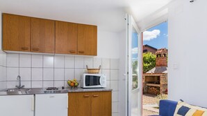 A compact kitchen with white cabinets, a microwave, and a sink. There's a basket of fruit on the counter and a blue sofa with a patterned cushion. - Cosy apartment for 3 guests with pool, A/C, WIFI, TV and terrace (Porec)