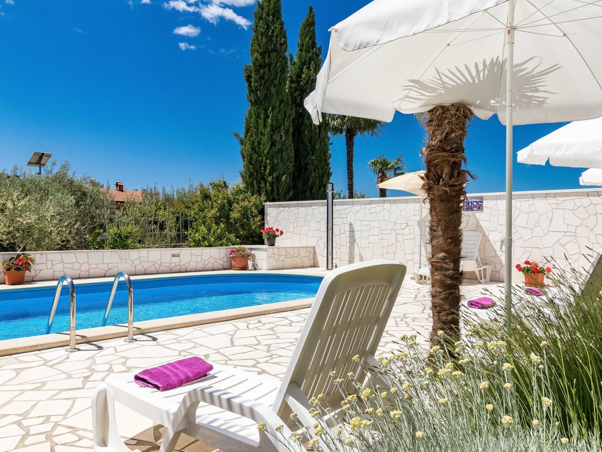 A pool area with a clear blue pool, white lounge chairs, and a white umbrella.