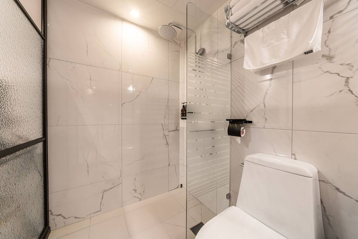 A modern bathroom with a glass shower enclosure, a toilet, and a towel rack.
