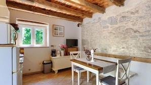 A kitchen with a wooden ceiling, a stone wall, a window with greenery outside, a TV, and a dining table with chairs.