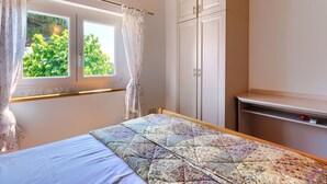 A bedroom with a bed, a window with curtains, a wardrobe, and a small shelf.