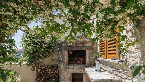A stone-built outdoor kitchen with a wood-fired oven, a stack of firewood, and a lantern.