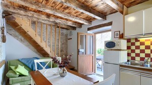 A cozy kitchen with a wooden ceiling, a dining area with a table and chairs, and a green sofa with cushions.