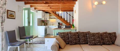 Ein gemütliches Wohnzimmer mit einer Couch, Sesseln, einer Treppe zu einer Küche und einem Essbereich.