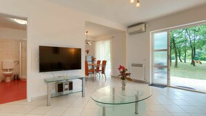 A modern living room with a flat-screen TV, a glass coffee table, and a dining area with orange chairs. - Nice apartment for 8 guests with A/C, WIFI, pool, TV and terrace (Pazin)